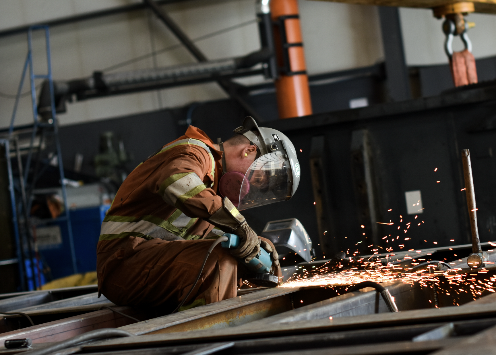 Travailleur en combinaison de sécurité utilisant une meuleuse dans un atelier industriel